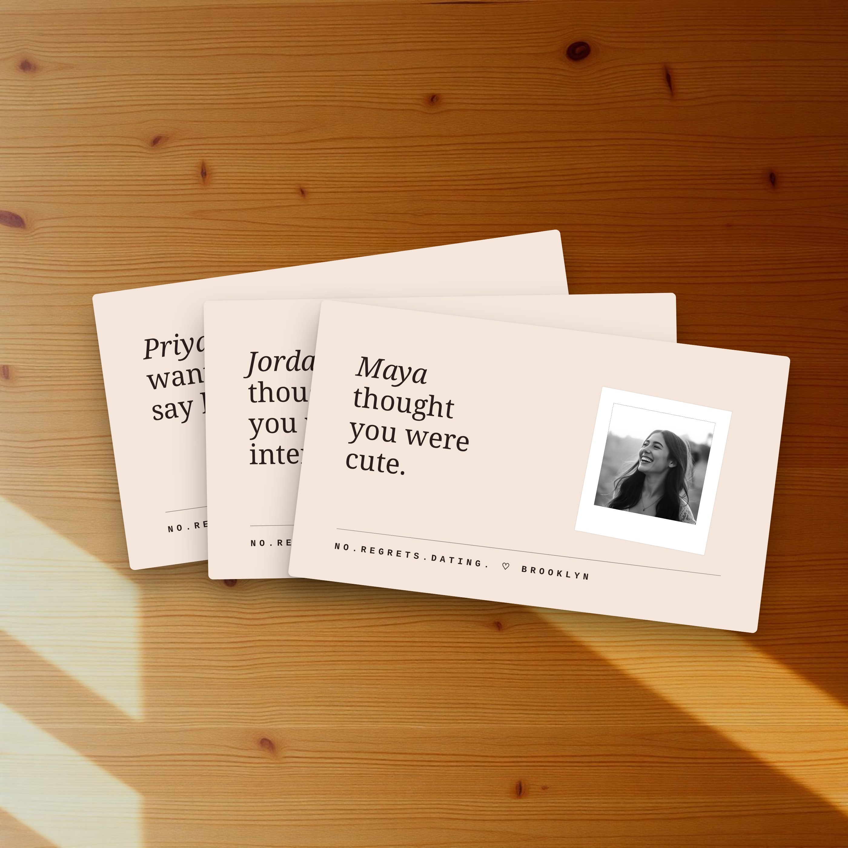 A tight fan of three No.Regrets.Dating. cards on a warm wood table, top card reads Maya thought you were cute.